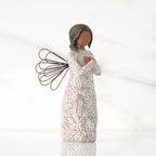 Facing right: angel with wire wings, darker skin, arms crossed over gold heart, dress carved with symbols of remembrance
