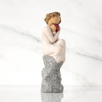 Facing right: figure in cream dress, seated on gray rock, knees drawn up to chest, holding red heart engraved with year 2023
