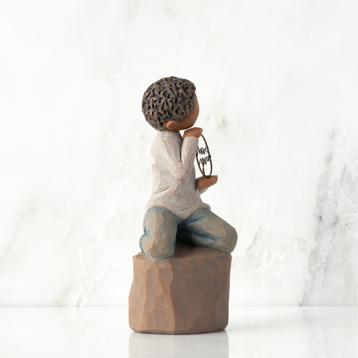 Left view: Figure of darker-skin child, kneeling on rock, holding wire circle with ‘love you’ written in wire