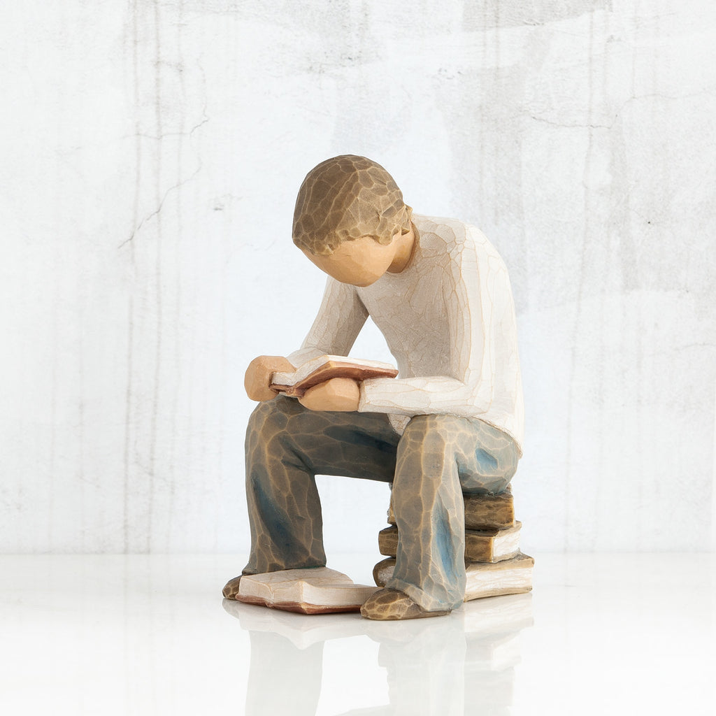 Young faceless boy figurine sitting on books with book opened in his hands - another book on the floor of his feet