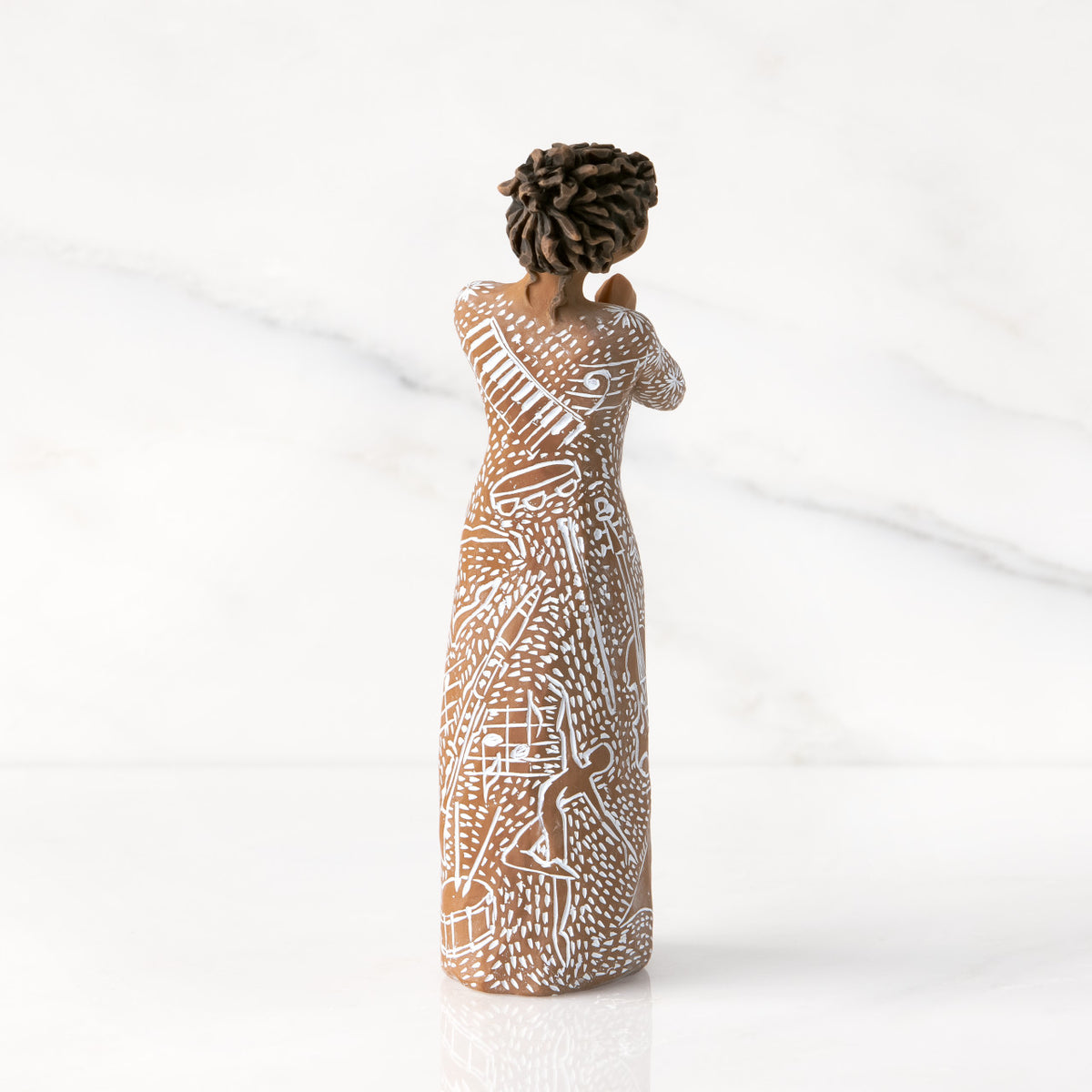 Back view: Darker-skin figure carved with contrasting pattern of white musical symbols, instruments, dancing forms