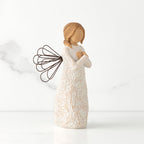 Right side view of standing female figure with wire wings in cream dress carved with natural symbols, hands crossed under gold heart on chest