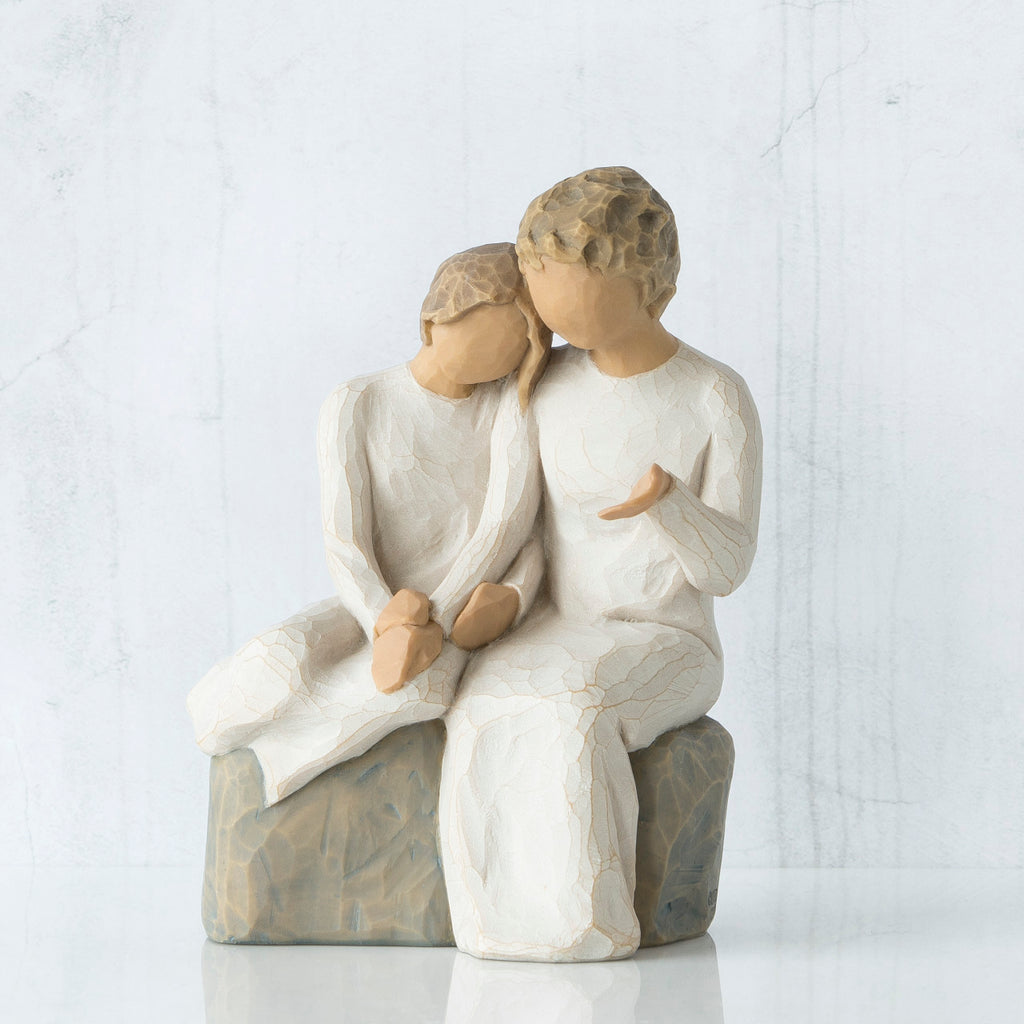Two faceless figurines wearing white sitting next to each other on rock