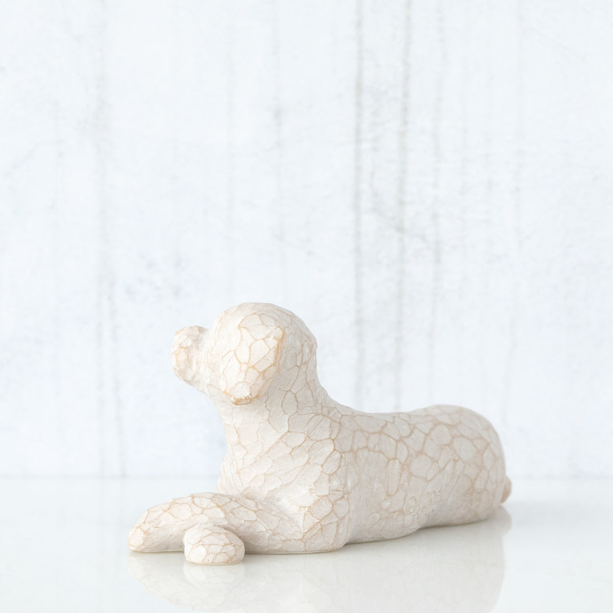 Figure of small white dog laying down with paws crossed in front, facing left
