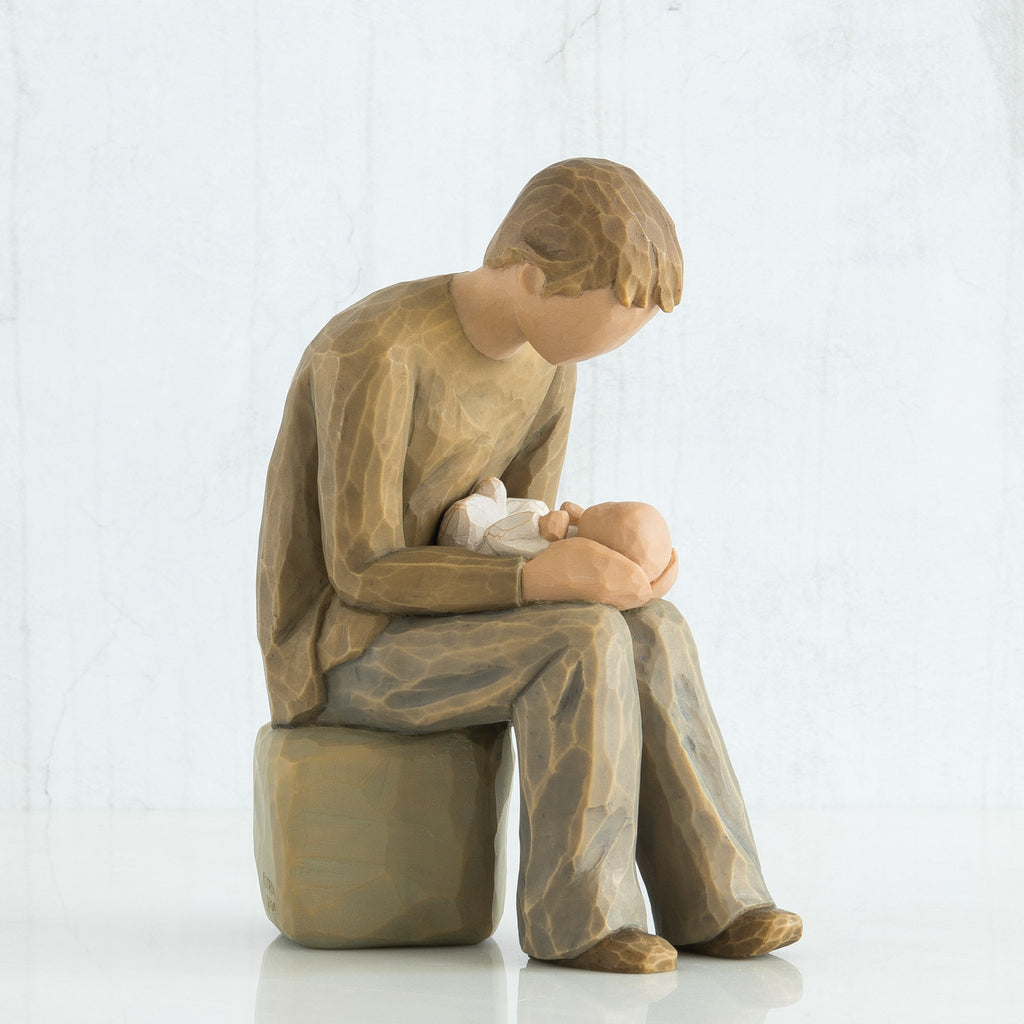 Man faceless figurine dressed in light brown sitting on rock holding baby in arms
