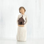 Faceless girl figurine facing forward wearing white dress, holding brown house figurine in her arms