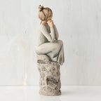 Brunette girl figurine sitting on grey  rock in grey dress with her hands up to her face