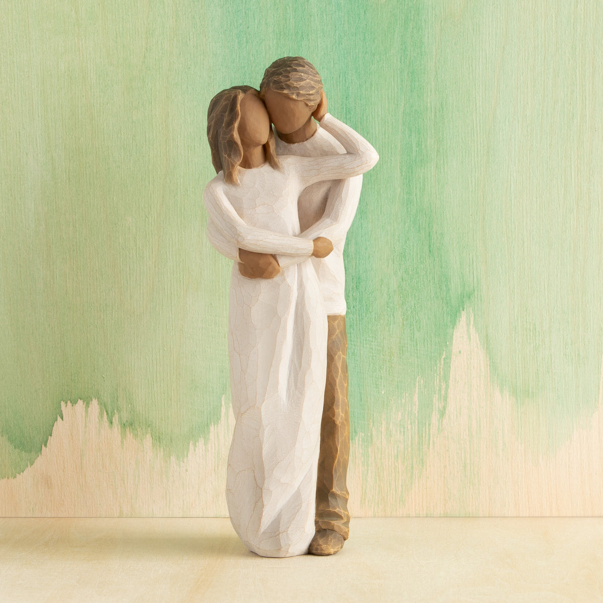 Front view of couple, standing with arms around each other. Woman and man have darker skin tones and hair color. Green painted background.