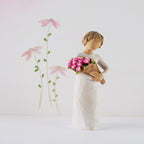 Willow Tree Bright Hope, 4”h hand-painted standing figure in cream dress, holding bouquet of bright pink tulips, in front of white painting