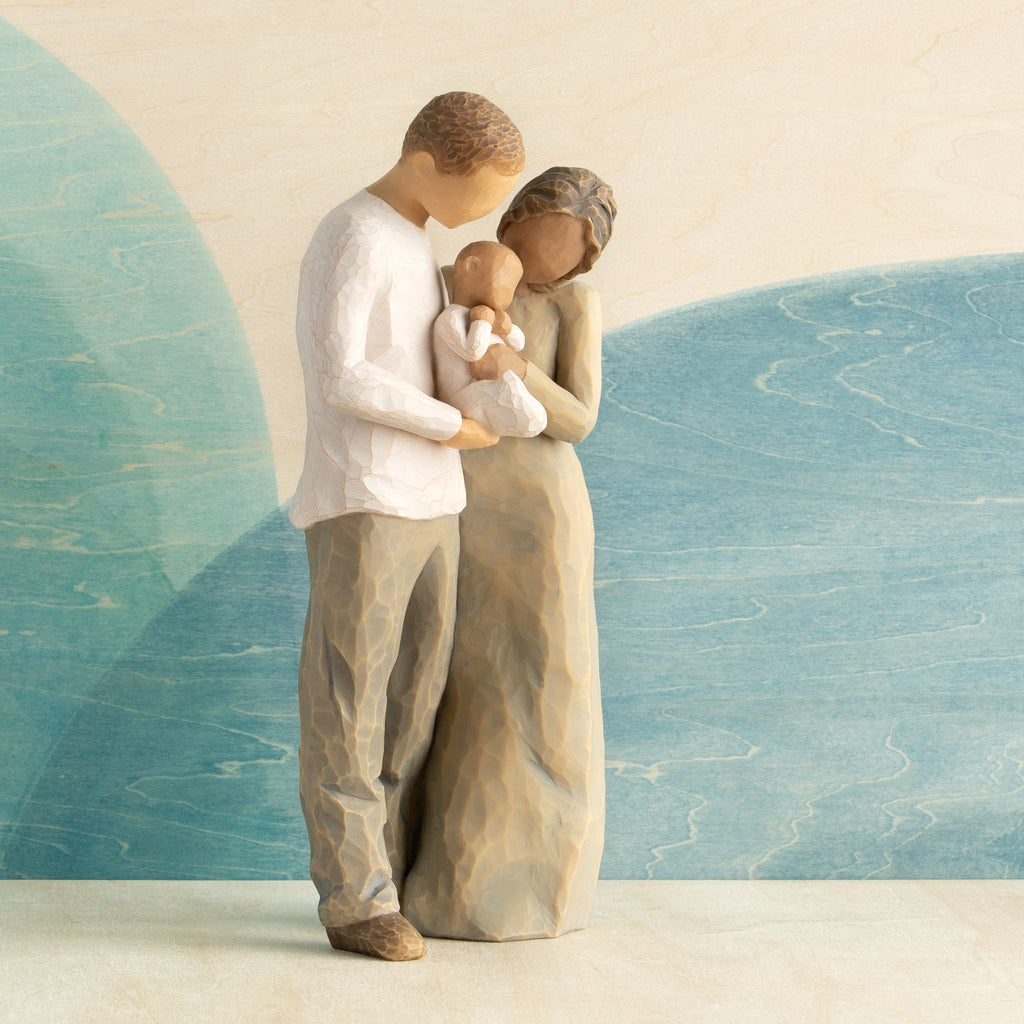 Front view of standing couple, woman has darker skin and hair; man has lighter skin and hair, holding a baby between them. Blue painted background.