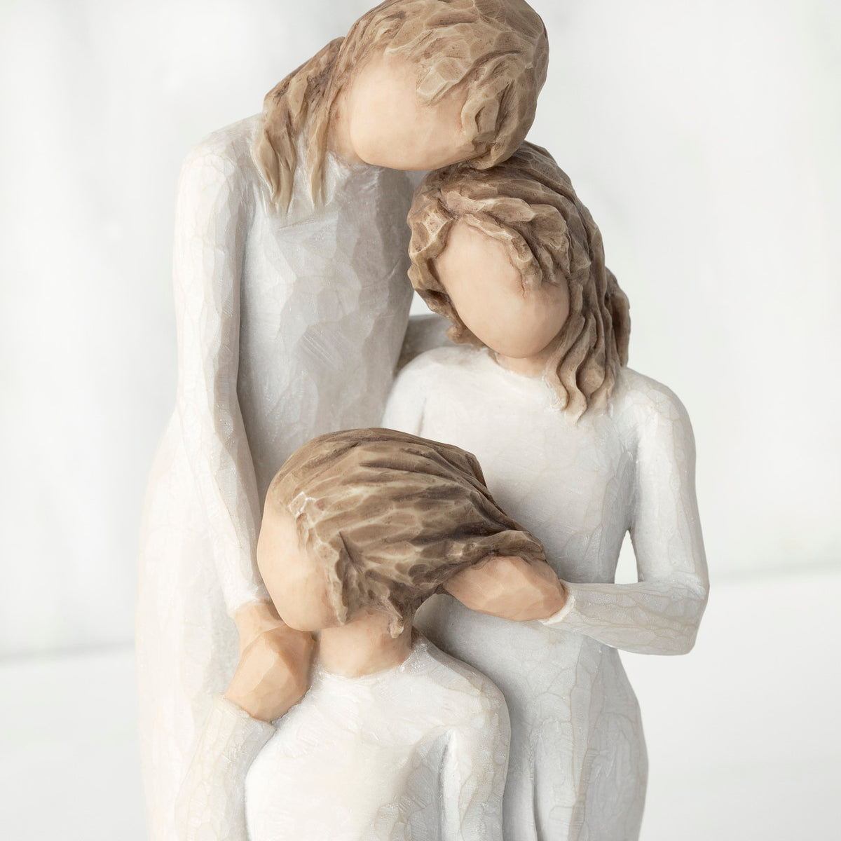 Close-up, cropped view, figurine of three females in cream dresses: one standing with arm around kneeling female, and holding hand of seated female