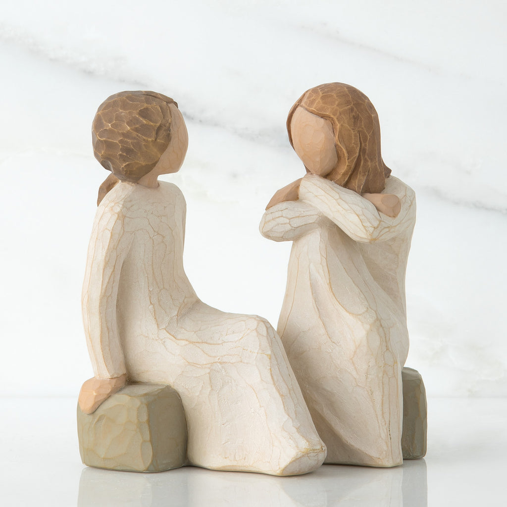 Two faceless girl figurines sitting on rocks facing each other - both wearing white dresses