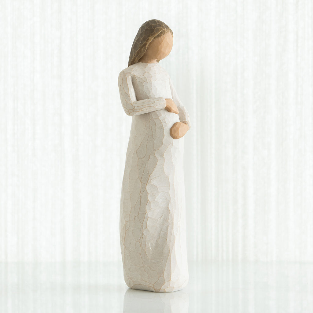 Faceless pregnant woman figurine wearing white dress with hands clutching her stomach