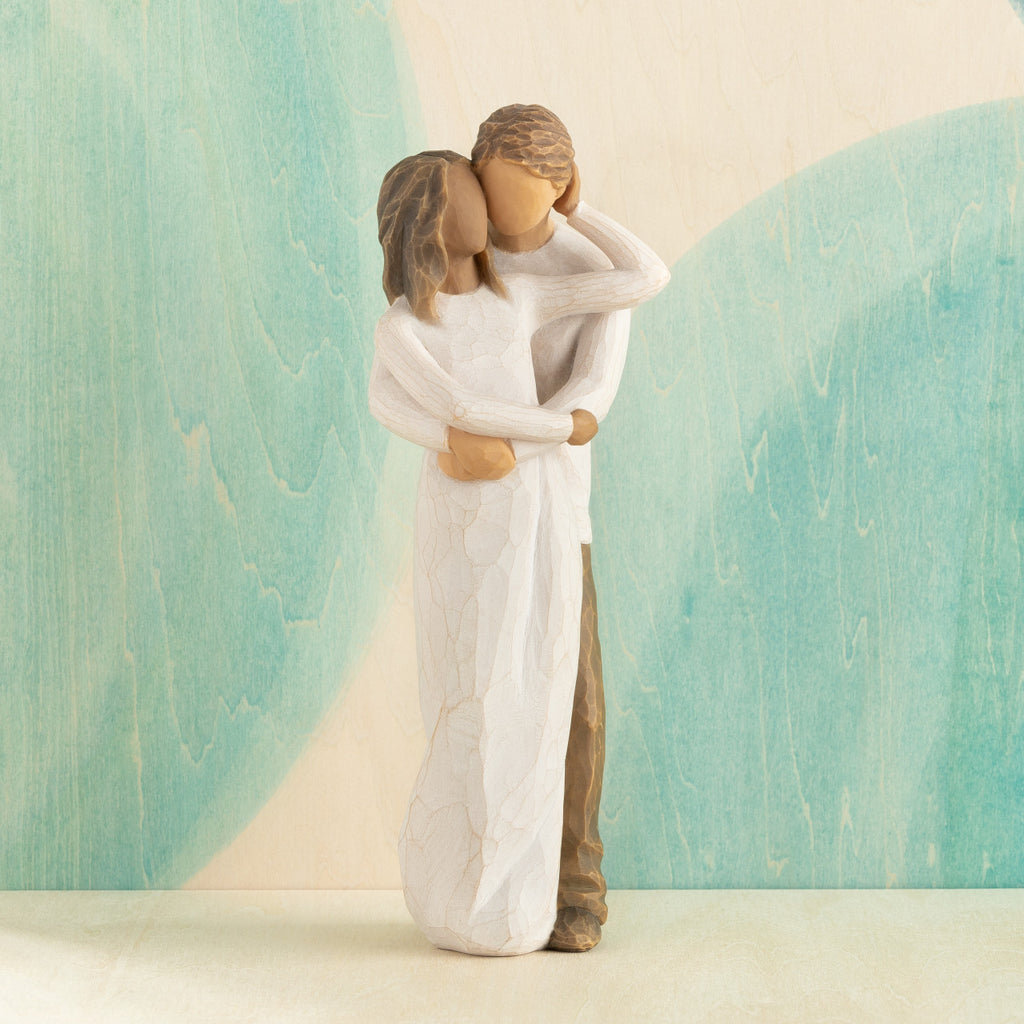 Front view of couple, standing with arms around each other. Woman has darker skin and hair; man has lighter skin and hair. Blue painted background.
