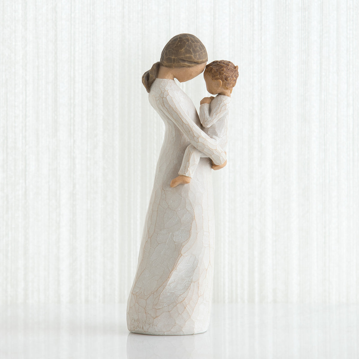 Side view of faceless mom figurine wearing white dress holding child in white outfit in her arms