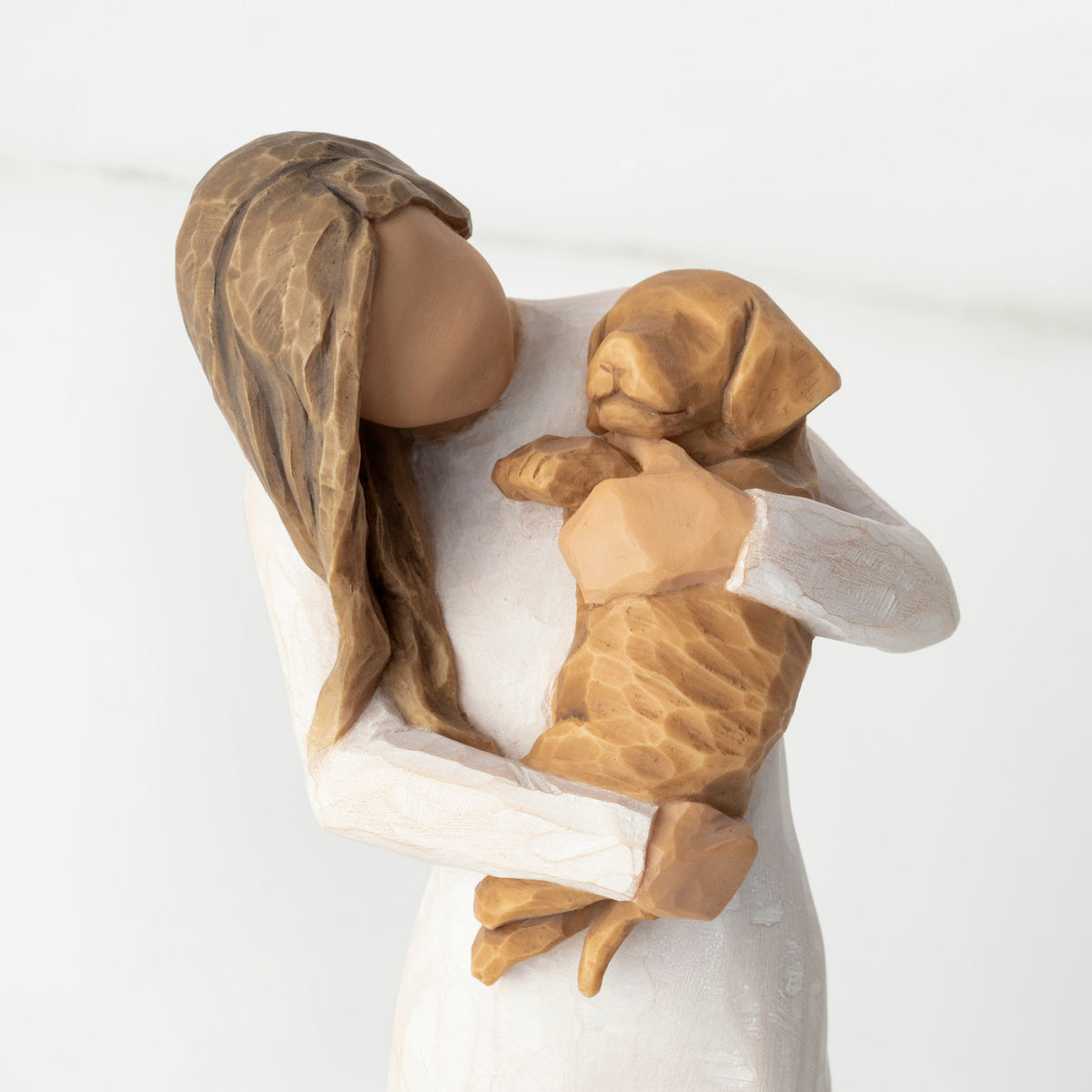 Close-up, cropped view of female figure in cream dress, holding golden color puppy in her arms