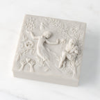 Closed white resin square box; lid carved with figural and organic imagery