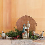 Far view of nativity scene figurines sitting on rock with brown barn in the background