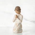 Small faceless girl figurine wearing white/tan bird design dress, kneeling and praying