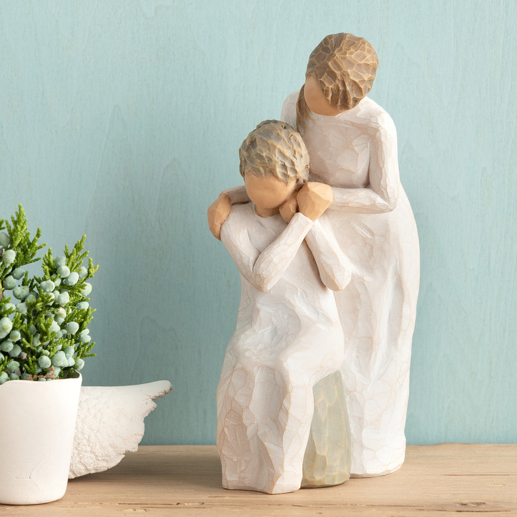 Willow Tree Loving My Mother, 6.5”h hand-painted resin figure of seated older woman with younger woman standing at her shoulder, both in cream dresses, hands clasped, in front of muted teal painting