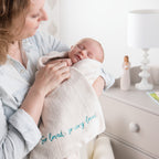 Side view of mother holding swaddled baby in light pink