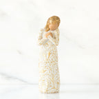 Faceless blonde woman figurine standing in white golden print dress clutching her hands to her chest
