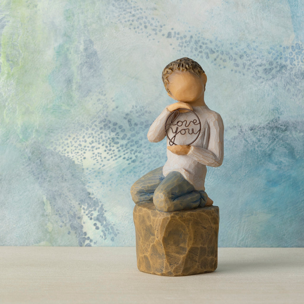 Willow Tree Love you too (lighter skin), 4.5”h hand-painted resin figure of young child in cream shirt and jeans, kneeling on rock, holding wire circle with ‘love you’ inside, in front of blue painting