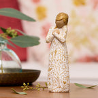 Willow Tree Tapestry, 5”h hand-painted standing resin figure, in cream dress, hands crossed at chest, entire figure carved with symbols of nature with gold-leaf, on table in warm light