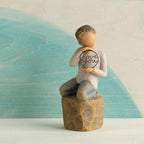 Willow Tree Love you too (lighter skin), 4.5”h hand-painted resin figure of young child in cream shirt and jeans, kneeling on rock, holding wire circle with ‘love you’ inside, in front of blue painting