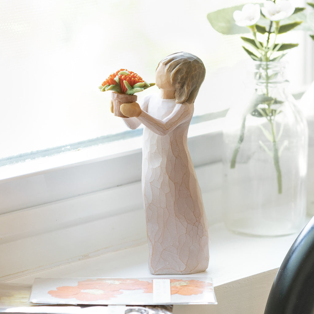 Willow Tree Little Things, 5.25”h hand-painted standing resin figure in cream dress, holding out terracotta pot with orange flowers, on bright windowsill