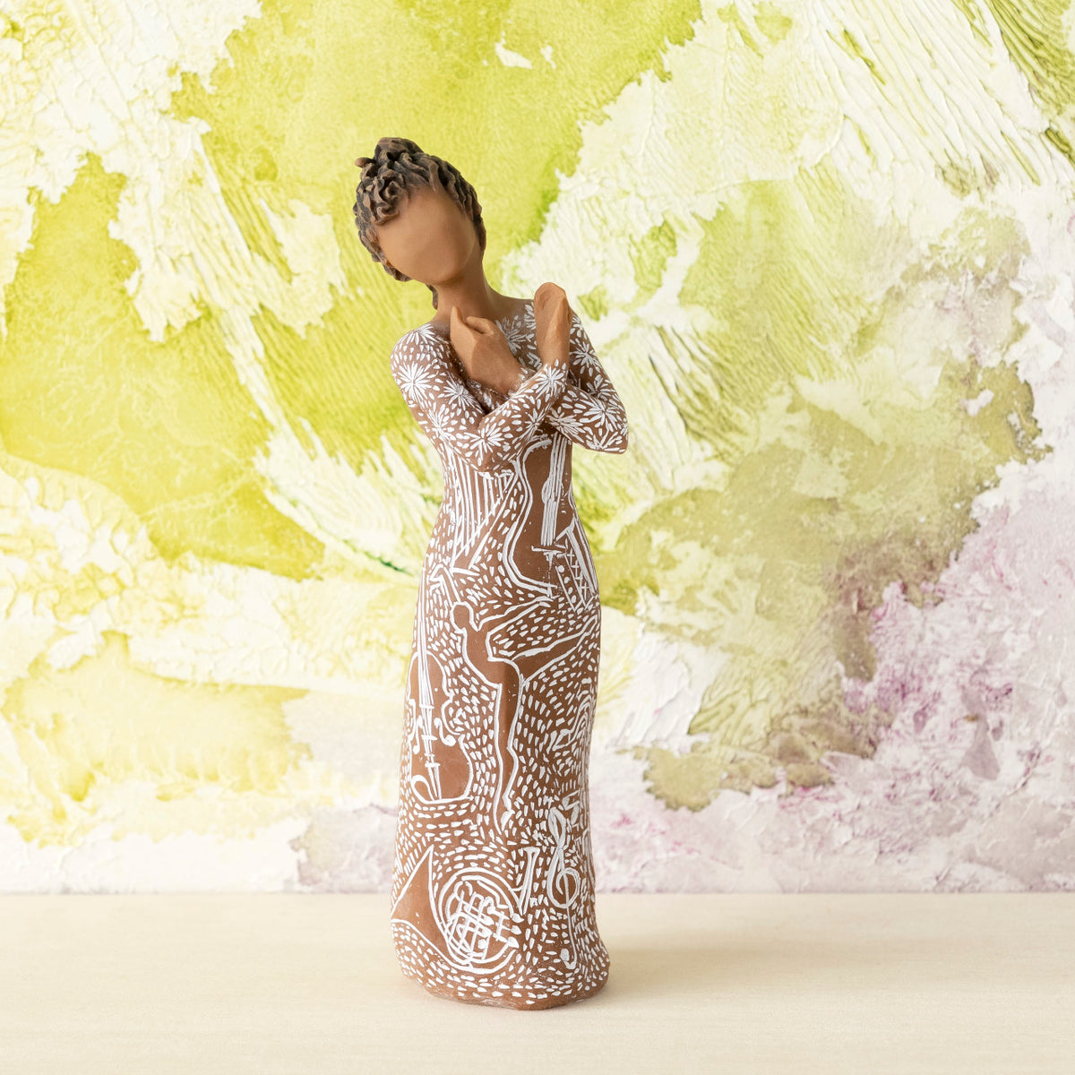 Willow Tree Music Speaks (darker skin), 7”h hand-painted standing resin figure, arms crossed, wearing dress carved with symbols of music and dancing, in front of lime green painting