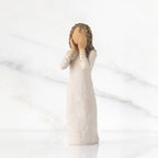 Front view: Standing figure in cream dress, both hands up to face, gold leaf dots on sleeves and throughout hair as a halo